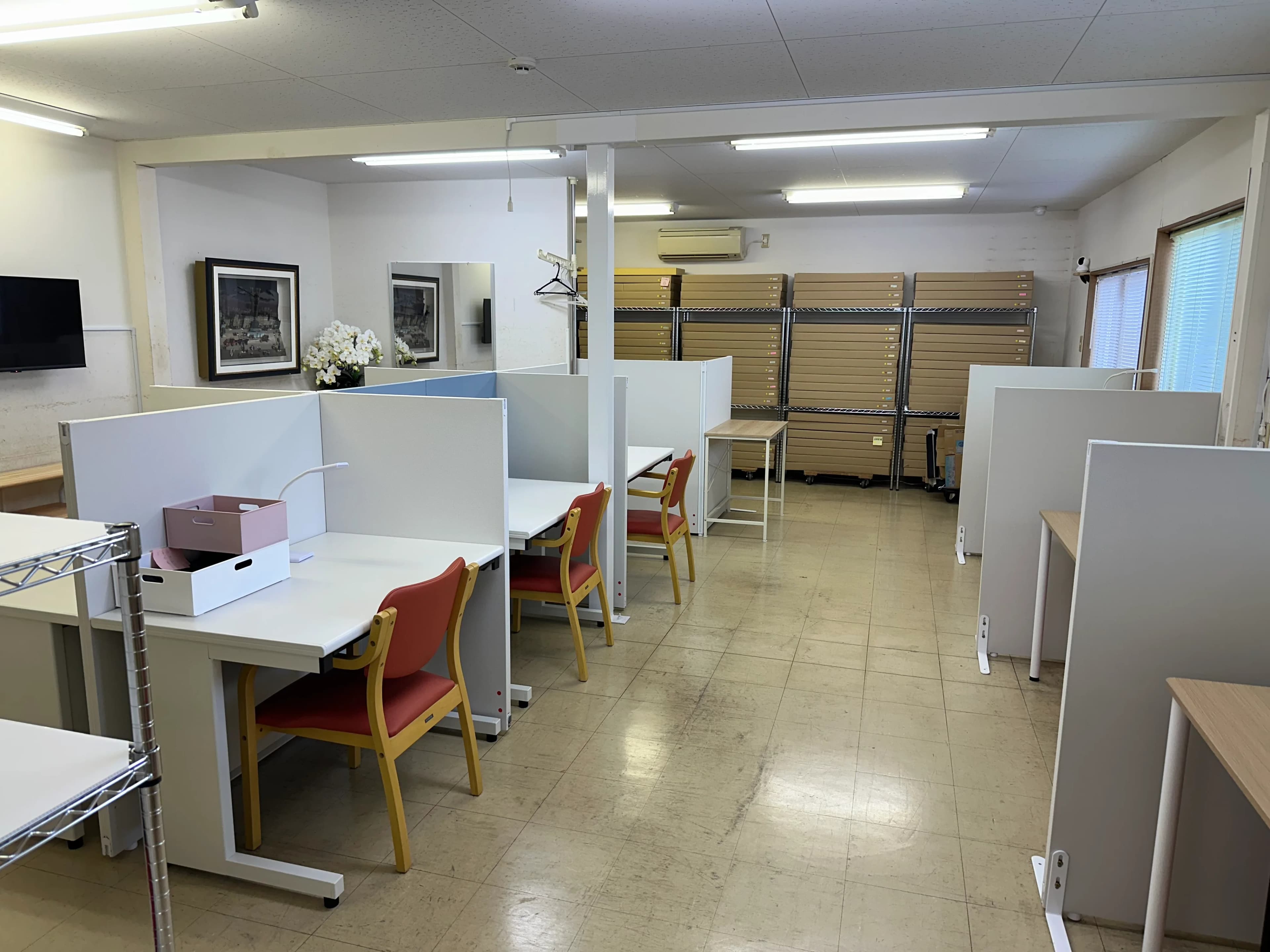 仕切り付きの机と赤い椅子が並ぶ作業室
